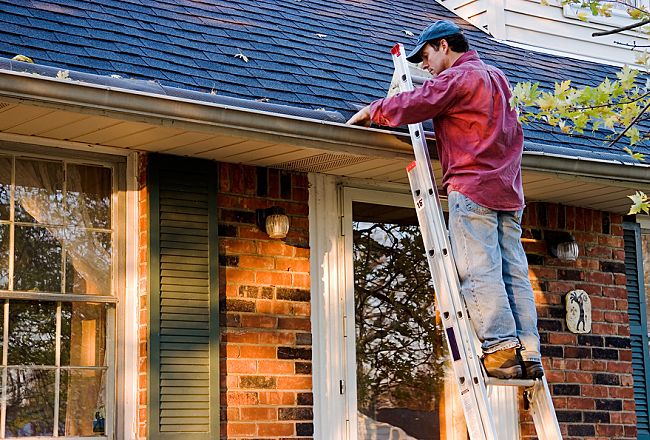 Person on a ladder cleaning gutters on a house